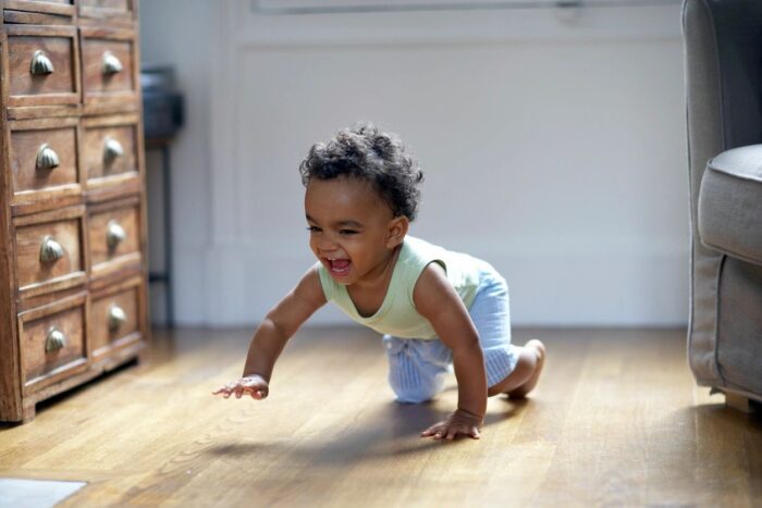 A baby is crawling on the floor in front of a wall.